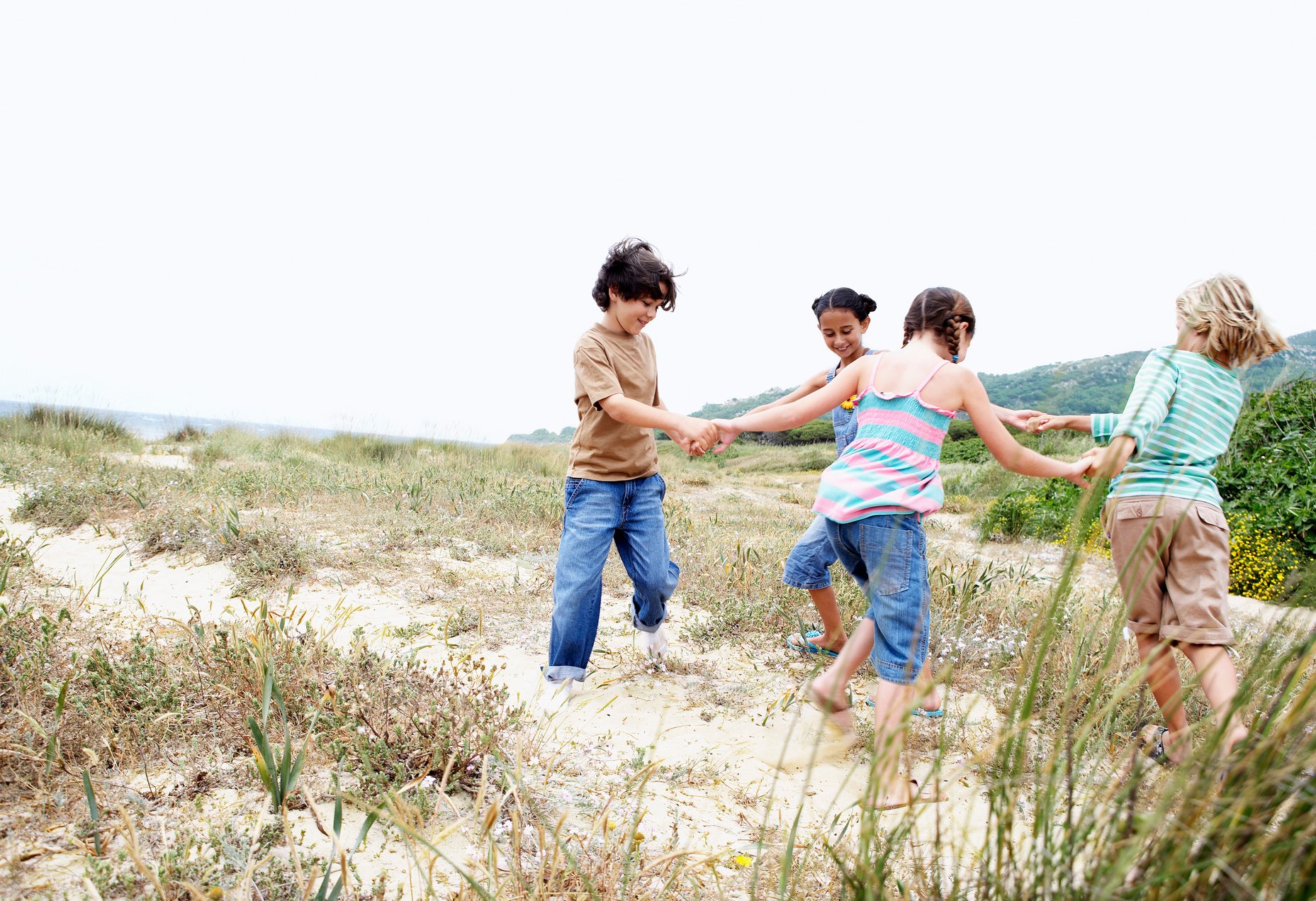 Children playing ring around the rosy on grassy beach